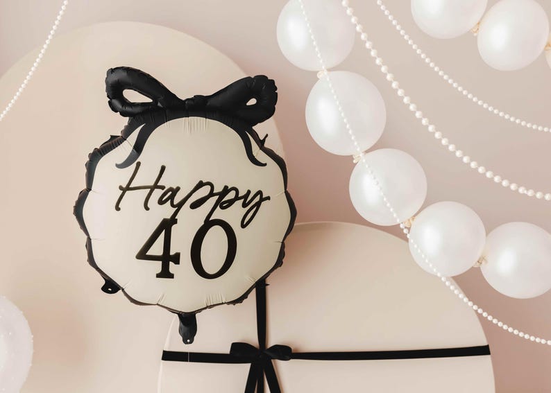 K&ouml;nnte beinhalten: Ein wei&szlig;er Ballon mit einem schwarzen Band und dem Text "Happy 40" in schwarzer Schrift. Der Ballon ist von wei&szlig;en Perlenketten umgeben.
