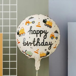Pode incluir: Um bal&atilde;o branco e amarelo com tema de constru&ccedil;&atilde;o com o texto "happy birthday" em preto. O bal&atilde;o apresenta ilustra&ccedil;&otilde;es de caminh&otilde;es de constru&ccedil;&atilde;o, cones e outros equipamentos de constru&ccedil;&atilde;o.