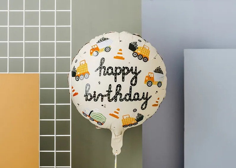 Pode incluir: Um bal&atilde;o branco e amarelo com tema de constru&ccedil;&atilde;o com o texto "happy birthday" em preto. O bal&atilde;o apresenta ilustra&ccedil;&otilde;es de caminh&otilde;es de constru&ccedil;&atilde;o, cones e outros equipamentos de constru&ccedil;&atilde;o.