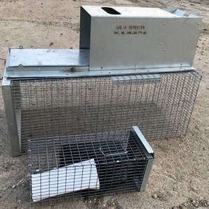 May include: A metal cage trap with a metal lid and a smaller cage trap attached to the side. The cage trap has a label that reads "LALIK REPEATER PAT. NO. 098448, 1997, AU".