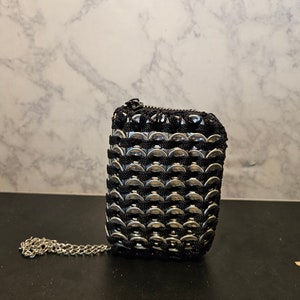 May include: A small black and silver purse made from woven pull tabs. The purse has a zipper closure and a silver chain strap.