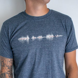 May include: A dark blue t-shirt with a white sound wave graphic on the front. The sound wave graphic is a visual representation of the phrase "Music is my therapy".