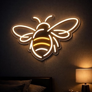 Pode incluir: Uma placa de néon em forma de abelha, com contorno branco e interior amarelo, está montada numa parede escura. As asas e o corpo da abelha estão claramente definidos, criando um efeito visual marcante. A placa é um elemento decorativo.