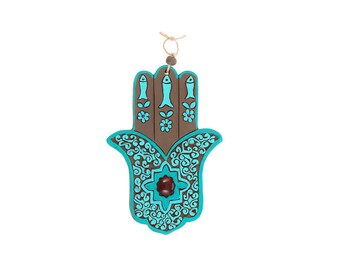 May include: A turquoise blue hamsa hand wall hanging with brown and white details. The hamsa hand has a red jewel in the center.
