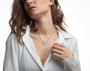 May include: A woman wearing a white collared shirt with a silver Star of David necklace.
