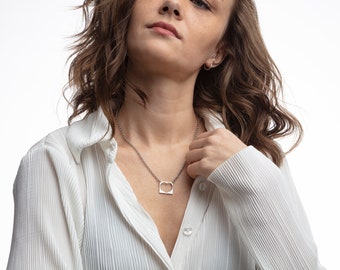 May include: A woman wearing a white collared shirt with a silver necklace featuring a heart-shaped pendant.