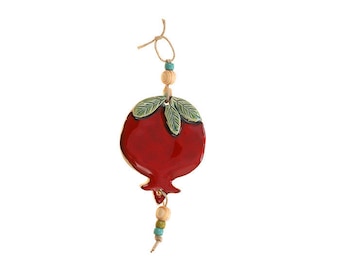 May include: A red ceramic pomegranate ornament with green leaves and a string of wooden and blue beads hanging from it.
