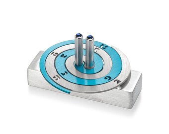 May include: A silver and blue metal dreidel with Hebrew letters and blue gemstones on the top. The dreidel is on a silver base.
