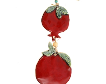 May include: A ceramic pomegranate wall hanging with two red pomegranates, green leaves, and wooden beads. The pomegranates are attached to a white ceramic branch with green leaves.