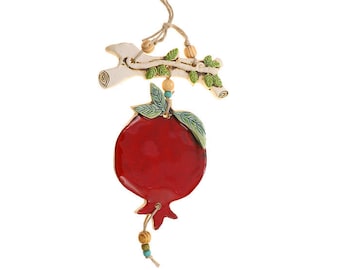 May include: A ceramic pomegranate ornament with a white branch and green leaves. The ornament is red and has a string for hanging.