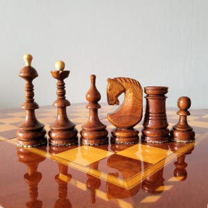 Può includere: Un set di sei pezzi degli scacchi in legno, tra cui un re, una regina, un alfiere, un cavallo, una torre e un pedone, sono disposti su una scacchiera a scacchi. I pezzi sono di colore marrone scuro con una finitura lucida.