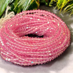 Könnte beinhalten: Nahaufnahme einer großen Spule mit rosa facettierten Glasperlen. Die Perlen sind klein und haben einen leichten irisierenden Schimmer.
