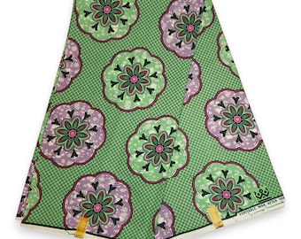 May include: Folded green fabric with a repeating floral pattern in shades of green, purple, and black. The fabric has a small dot pattern in the background. The fabric is labeled "VERITABLE WAX MITEX HO".