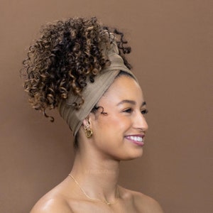 Peut inclure: Une femme aux cheveux bruns bouclés porte un turban brun. Elle sourit et regarde vers la droite. Elle porte un collier en or et des boucles d'oreilles créoles en or.