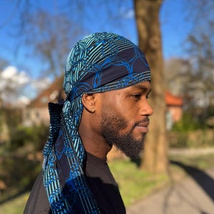 Puede incluir: Un hombre con un turbante de patrón azul y negro. El turbante tiene un diseño geométrico con círculos y líneas.