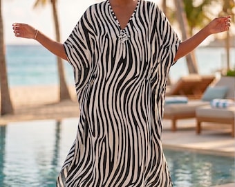 Puede incluir: Un vestido caftán con estampado de cebra en blanco y negro con escote en V. El vestido tiene una silueta suelta y fluida y está hecho de una tela ligera. El caftán es adecuado para ropa de playa o de resort.