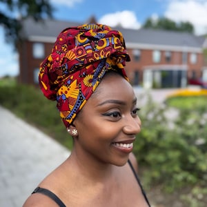 Op de afbeelding: Een levendige hoofdwikkel met een kleurrijk geometrisch patroon in rood, geel, blauw en paars. De hoofdwikkel is om het hoofd gewikkeld en creëert een stijlvol en opvallend accessoire. De hoofdwikkel is een gedurfd statement-stuk.