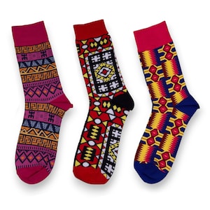 Peut inclure: Trois paires de chaussettes colorées avec des motifs géométriques. Les chaussettes sont rouges, bleues et roses avec des accents jaunes, noirs et blancs.
