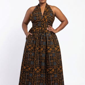 Könnte beinhalten: Ein bodenlanges Neckholder-Kleid mit einem geometrischen, von Mudcloth inspirierten Muster in Schwarz, Braun und Weiß. Das Kleid hat einen tiefen V-Ausschnitt, ein eng anliegendes Oberteil mit breitem Bund und einen weiten, plissierten Rock mit Seitentaschen.
