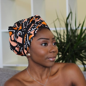 Puede incluir: Una mujer con un turbante de tela negra, naranja y rosa con estampado.