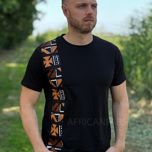 Puede incluir: Camiseta negra con un panel vertical decorativo en el lado izquierdo con patrones geométricos en marrón, blanco y negro. El texto "AFRICANFABS" está impreso en el lado derecho de la camiseta. La camiseta es de manga corta.