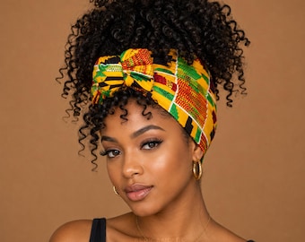 Puede incluir: Un pañuelo para la cabeza con un vibrante patrón inspirado en el Kente en amarillo, verde, rojo y negro. La tela está atada en un nudo en la parte delantera, asegurando un peinado voluminoso con rizos apretados. El accesorio se lleva alrededor de la cabeza.