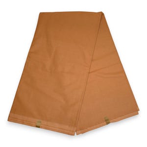 Op de afbeelding: Een gevouwen stuk effen bruine stof met een gladde, matte textuur. Het textiel is in een driehoekige vorm gerangschikt en vertoont een consistente, warme bruine kleur over het gehele oppervlak, met zichtbare rechte randen en nette naden.