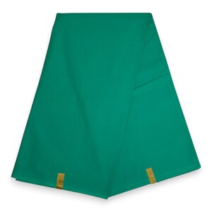 Op de afbeelding: Een effen smaragdgroene stof gevouwen in een driehoekige vorm. Het textiel heeft een gladde, matte oppervlaktestructuur en bevat twee kleine, rechthoekige goudkleurige stoffen lipjes bevestigd aan de onderranden van het materiaal.