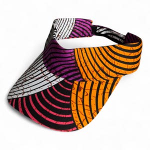 Op de afbeelding: Een kleurrijk vizier met een patchwork-ontwerp. Het vizier heeft een mix van patronen, waaronder witte strepen, gebogen lijnen in oranje en zwart en roze en paarse gebogen lijnen. Het vizier heeft een zwarte verstelbare band.