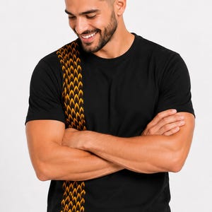 Op de afbeelding: Een zwart T-shirt met korte mouwen en een verticaal paneel aan de rechterkant, versierd met een herhalend oranje en zwart schubpatroon. Het kledingstuk is voorzien van een klassieke ronde hals en een effen zwarte achterkant.