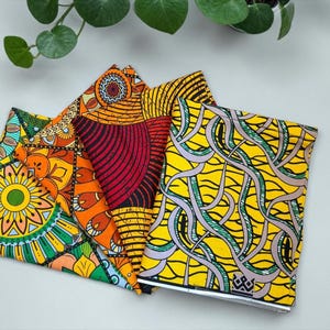 Op de afbeelding: Vier kleurrijke notitieboekjes met levendige Afrikaanse waxprint ontwerpen. De notitieboekjes hebben patronen in geel, oranje, rood en groen. De ontwerpen omvatten geometrische vormen en bloemmotieven, wat een opvallende collectie creëert.