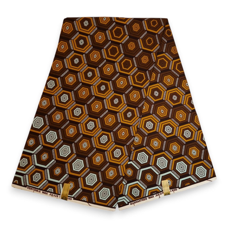 Może przedstawiać: Złożona tkanina z powtarzającym się geometrycznym wzorem brązowych, złotych i białych sześciokąt&oacute;w. Tkanina ma woskowe wykończenie, a na krawędziach nadrukowano tekst "VERITABLE WAX JULIUS" i "GUARANTEED WAX JULIUS".