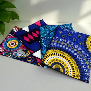 Op de afbeelding: Een verzameling kleurrijke stoffen vierkanten met levendige patronen. De ontwerpen omvatten bloemen-, geometrische en abstracte motieven in blauw, roze, geel en wit. De stoffen zijn in een waaier gerangschikt.
