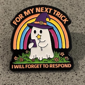 Peut inclure: Épinglette noire avec un fantôme blanc portant un chapeau de sorcière violet, tenant un téléphone et une baguette étoile. L'épinglette présente un arc-en-ciel et le texte "FOR MY NEXT TRICK I WILL FORGET TO RESPOND" en orange et blanc.