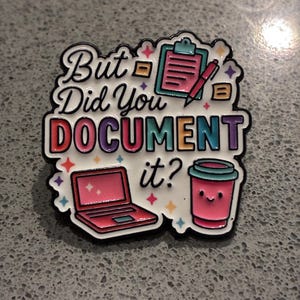 May include: A white enamel pin featuring the black text But Did You DOCUMENT it? surrounded by colourful illustrations of a pink clipboard with a pen, a pink laptop, and a pink coffee cup with a smiling face, accented by small multicoloured stars.