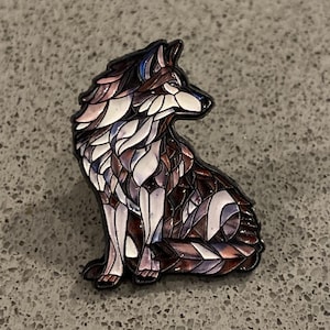 Peut inclure: Une épingle en émail détaillée représentant un loup assis. L'épingle présente un motif de style vitrail avec des nuances de marron, de blanc et de violet. Le loup a un contour noir et se détache sur un fond gris.