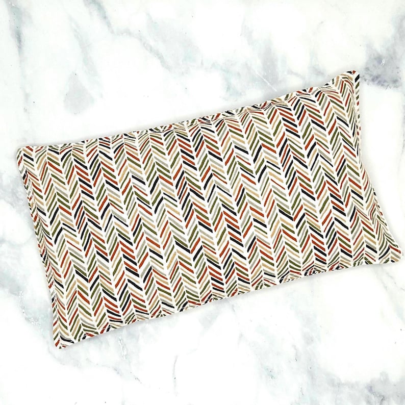 A rectangular rice eye pillow with a white background and a herringbone pattern in shades of green, brown, orange, and black.