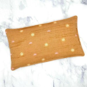 A mustard gold rectangular rice eye pillow with a repeating pattern of yellow suns and sunrises.