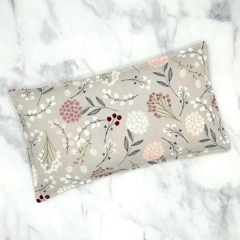 A grey rectangular rice bag pillow with a floral pattern. The pattern features white, pink, and burgundy flowers and leaves on a light grey background.