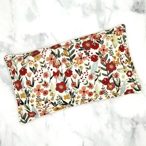 A rectangular floral print rice heat pack. The print features burgundy, pink, and gold flowers on a white background.