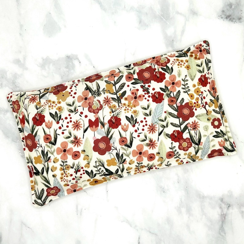 A rectangular floral print rice heat pack. The print features burgundy, pink, and gold flowers on a white background.