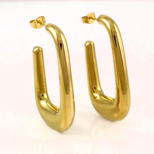 May include: A pair of gold-coloured, rectangular hoop earrings. The earrings have a polished finish and a post-and-clasp closure. The hoops are approximately 3.8 cm long and 1.9 cm wide.