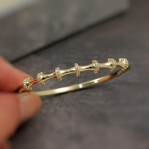 May include: A gold-coloured bangle bracelet with a bamboo-inspired design. The bracelet features a series of connected segments, each adorned with small, sparkling embellishments. The overall design is elegant and delicate, suitable for everyday wear or special occasions.