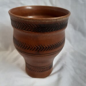 May include: A brown ceramic mug with a decorative pattern of black arrows around the middle.