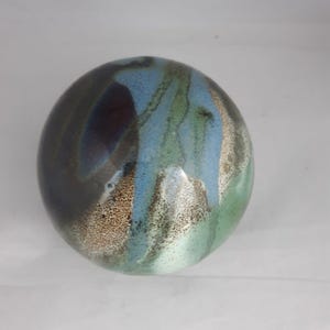 Peut inclure: Un objet décoratif rond en céramique avec un mélange de couleurs. Le dessus présente une zone marron foncé et bleue, passant au bleu clair et au vert avec une section tachetée de couleur beige. L'émail a un effet dégoulinant.