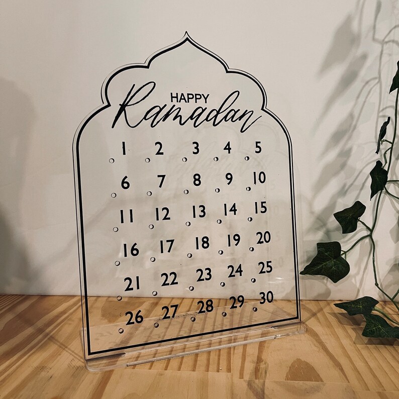 K&ouml;nnte beinhalten: Ein transparenter Ramadan-Kalender aus Acryl mit schwarzem Rahmen und dem Schriftzug "Happy Ramadan" oben. Der Kalender hat 30 nummerierte Kreise f&uuml;r jeden Tag des Monats.