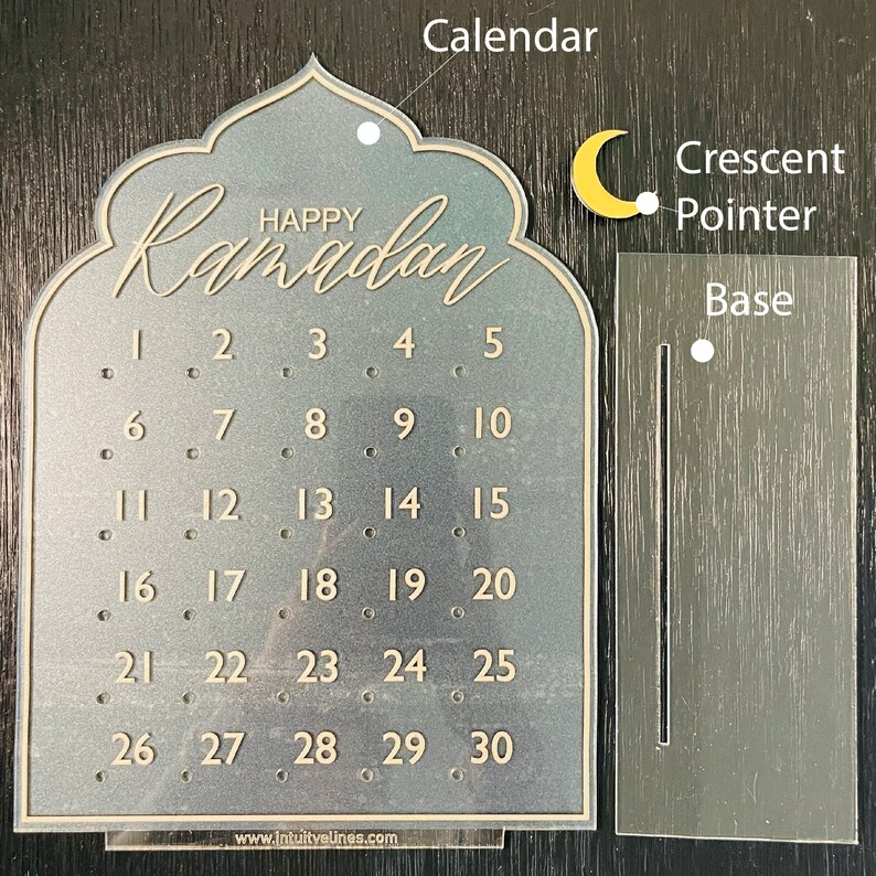K&ouml;nnte beinhalten: Ein transparenter Ramadan-Kalender aus Acryl mit einem Halbmondzeiger und einem Sockel. Der Kalender zeigt die Zahlen von 1 bis 30 und den Text "Happy Ramadan".