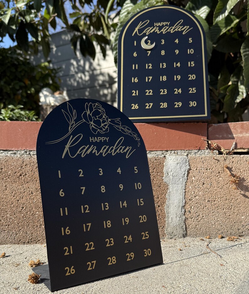 K&ouml;nnte beinhalten: Schwarzer Ramadan-Kalender aus Holz mit goldener Beschriftung und einem Halbmond-Design. Der Kalender zeigt ein florales Design und die Worte "Frohes Ramadan".
