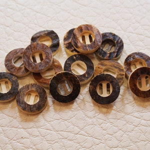 May include: A collection of brown and beige round buttons with a hole in the center. The buttons are made of natural materials and have a rustic look.