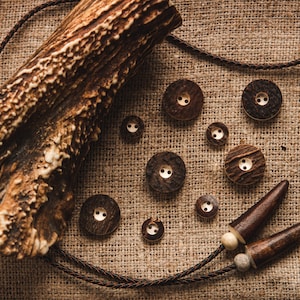 Puede incluir: Una colección de botones de madera marrón con una cornamenta natural y un cordón de cuero marrón sobre un fondo de arpillera.